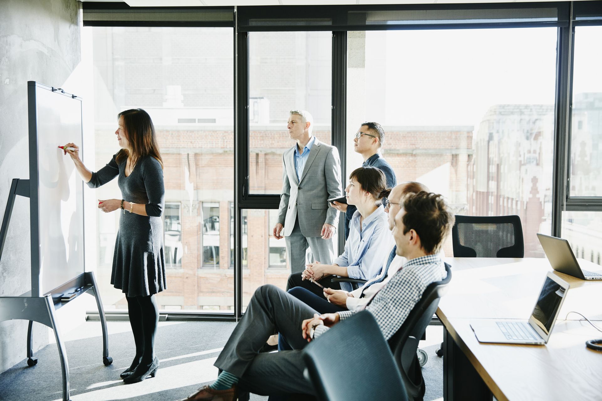 A woman leading a discussion at a Kapsch TrafficCom event, standing in front of a group of people.