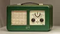 Radio verde con botones y perillas, representando la innovación de Kapsch en la producción de la primera radio portátil de transistores.