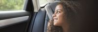 Eine Frau in einem Auto, die aus dem Fenster schaut, symbolisiert die Vision und Mission von Kapsch TrafficCom für innovative Mobilitätslösungen.