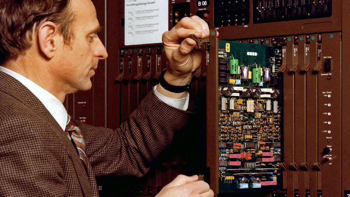 Un hombre reparando una computadora en un contexto histórico de innovación tecnológica de Kapsch.