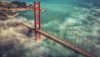 Eine Hängebrücke mit Autos darauf, umgeben von Wolken und Wasser.