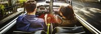 Couple driving convertible on city boulevard KTC3254-1920x656