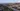 © Kapsch TrafficCom Luftaufnahme einer Autobahn in einer Stadt mit umgebenden Gebäuden und Bergen im Hintergrund.