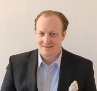 A smiling man in a suit with a blazer and dress shirt.