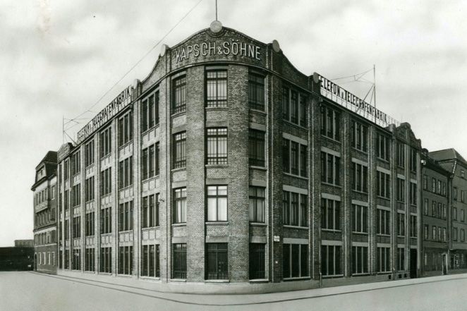 Schwarzweißfoto eines großen Gebäudes mit markanter Fassade und zahlreichen Fenstern, aufgenommen bei bewölktem Himmel.