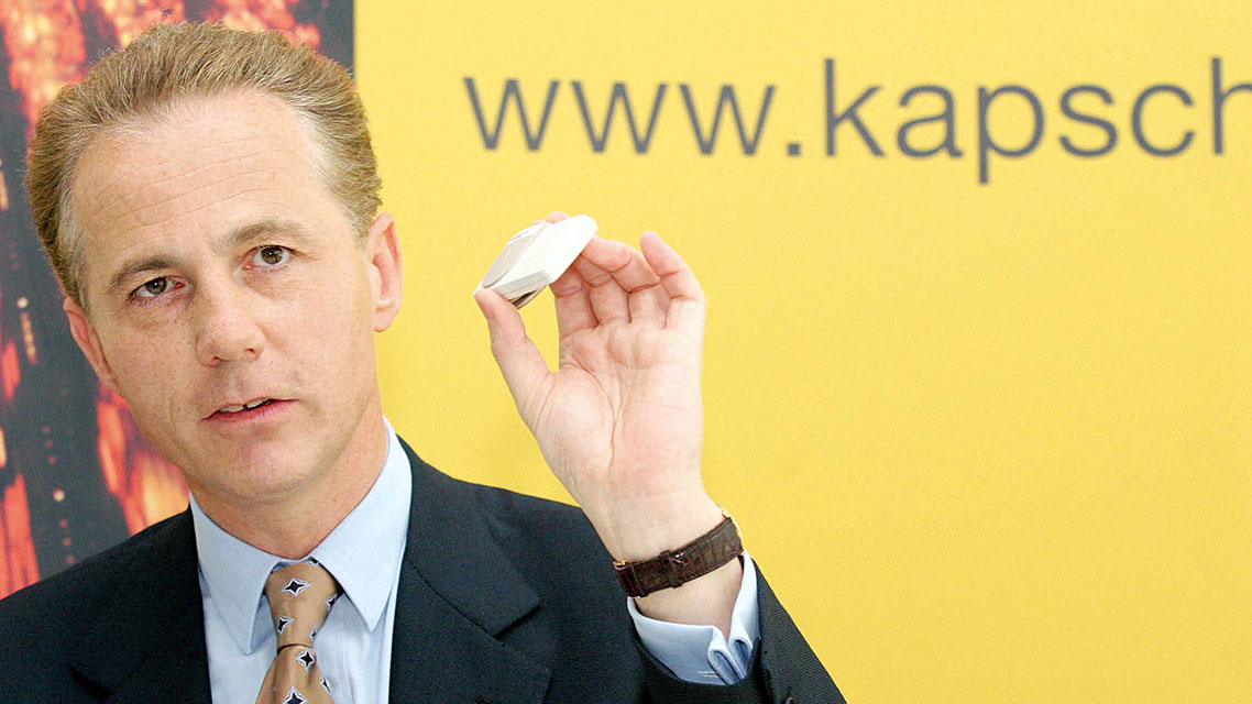 Un hombre con traje sosteniendo un pequeño objeto, representando la historia empresarial de Kapsch.