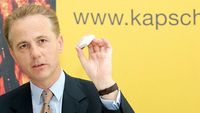 Ein Mann in Anzug hält ein kleines Objekt in der Hand.
