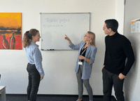 Eine Gruppe von Menschen steht vor einem Whiteboard.