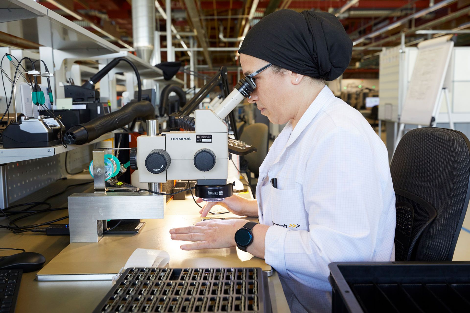Eine Technikerin bei Kapsch Components blickt durch ein Mikroskop in einem Labor.