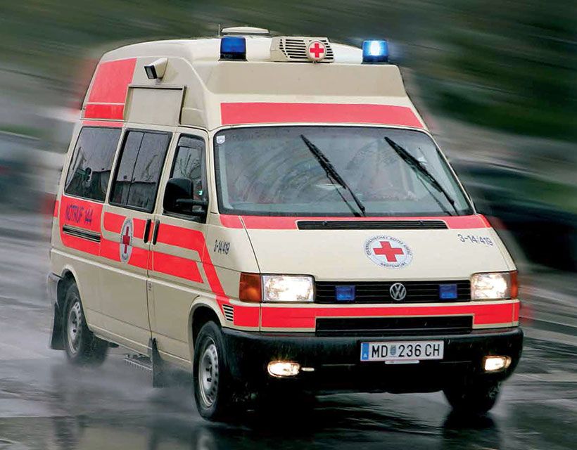 Eine rot-weiße Ambulanz auf einer nassen Straße.